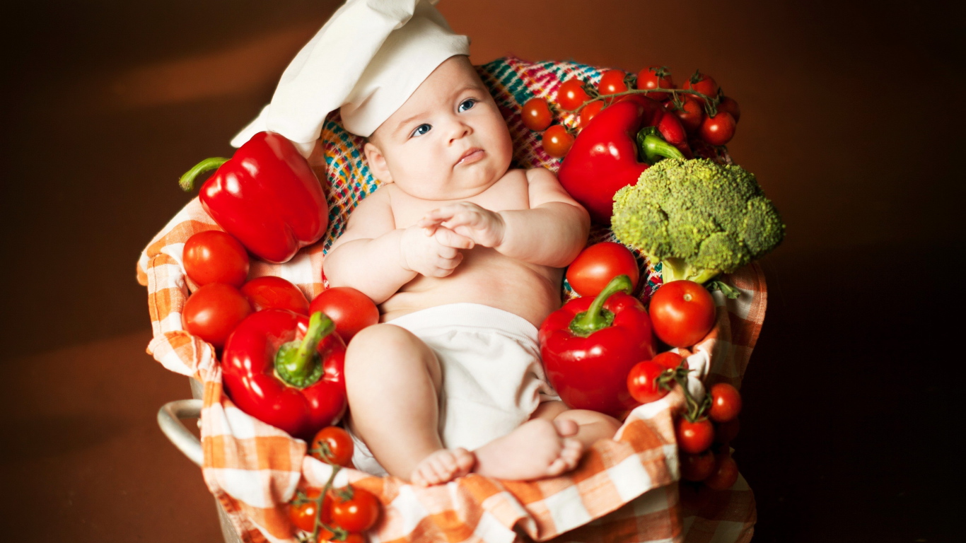 Маленький мальчик в костюме повара в корзине с перцем и помидорами
