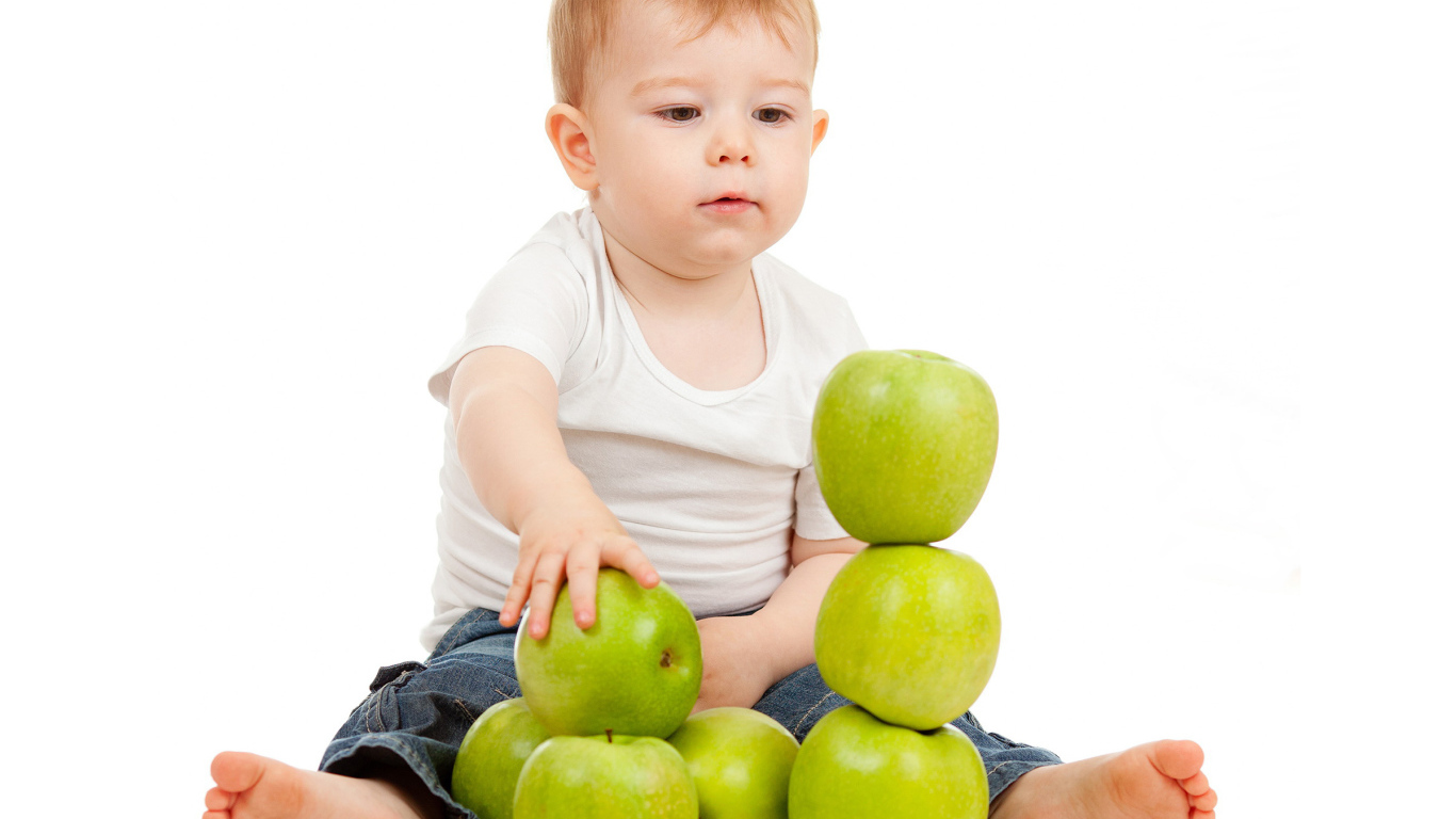 Маленький мальчик играет с зелеными яблоками на белом фоне