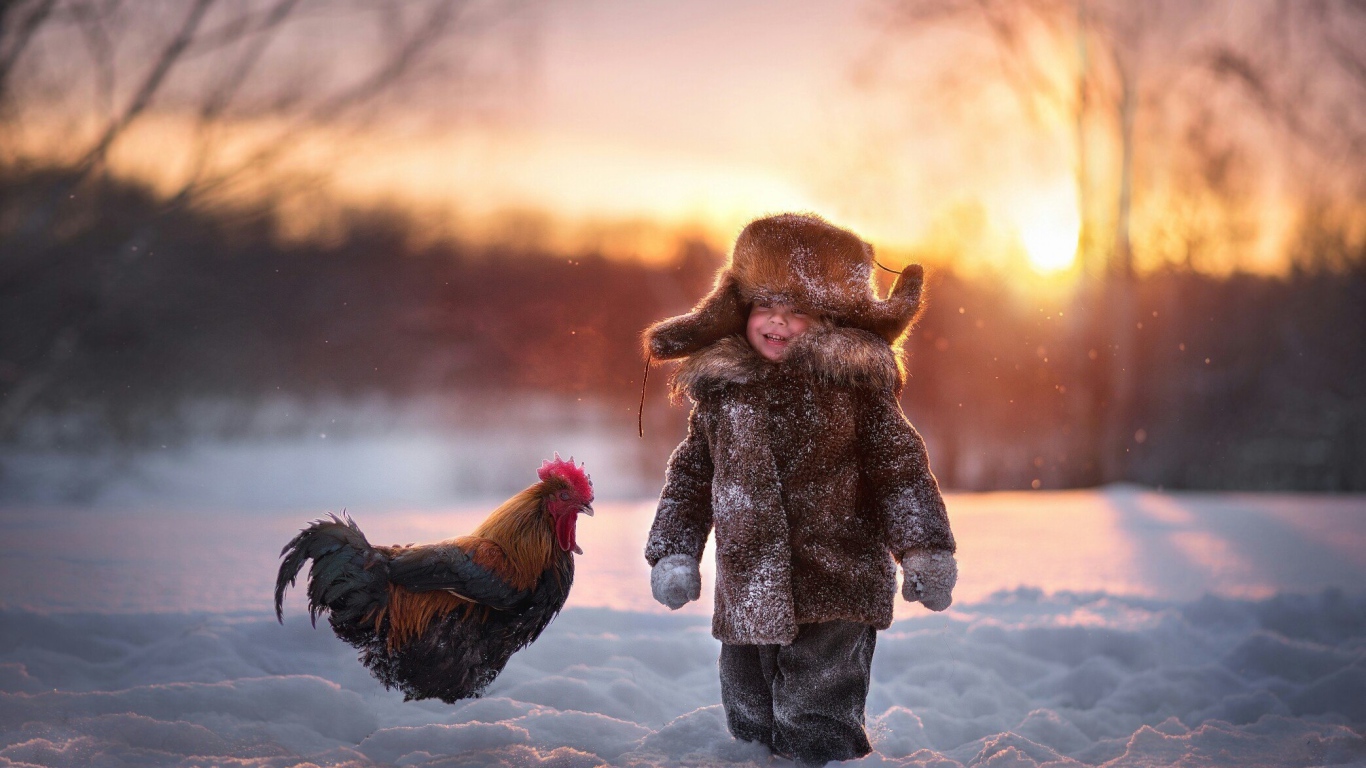 Маленький мальчик с петухом на снегу зимой