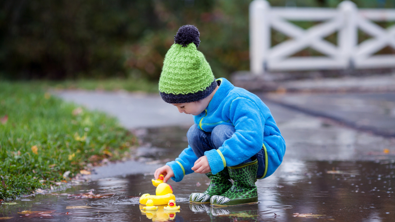 Маленький мальчик с резиновыми уточками в луже осенью