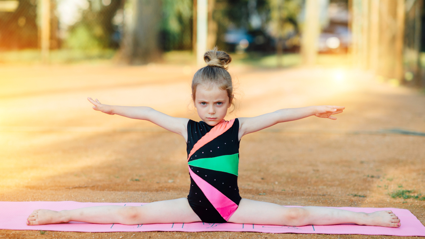 Маленькая девочка гимнастка сидит на шпагате 