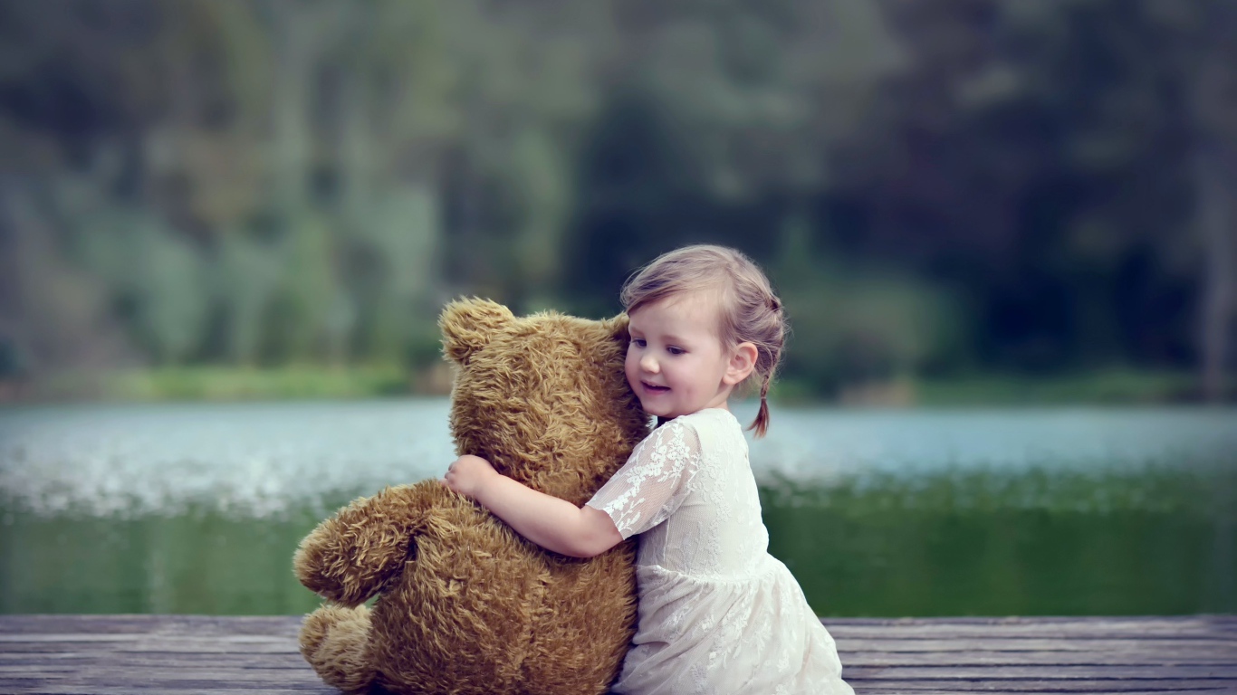 Маленькая девочка в белом платье сидит на мосту с плюшевым медведем
