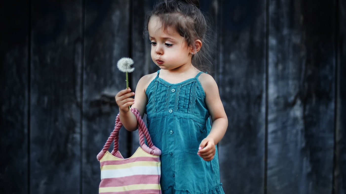 Маленькая девочка с сумкой и одуванчиком в руке