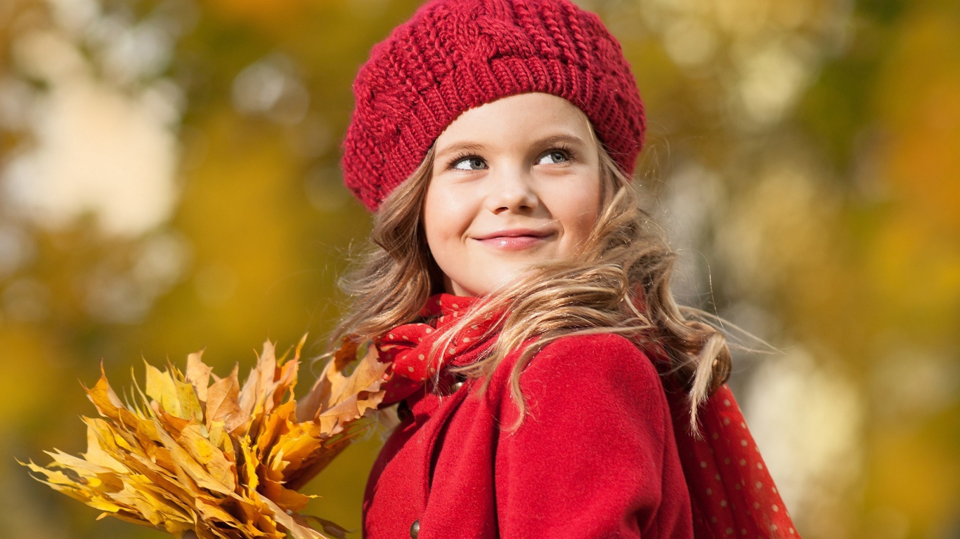 Маленькая девочка с желтыми листьями в руке осенью