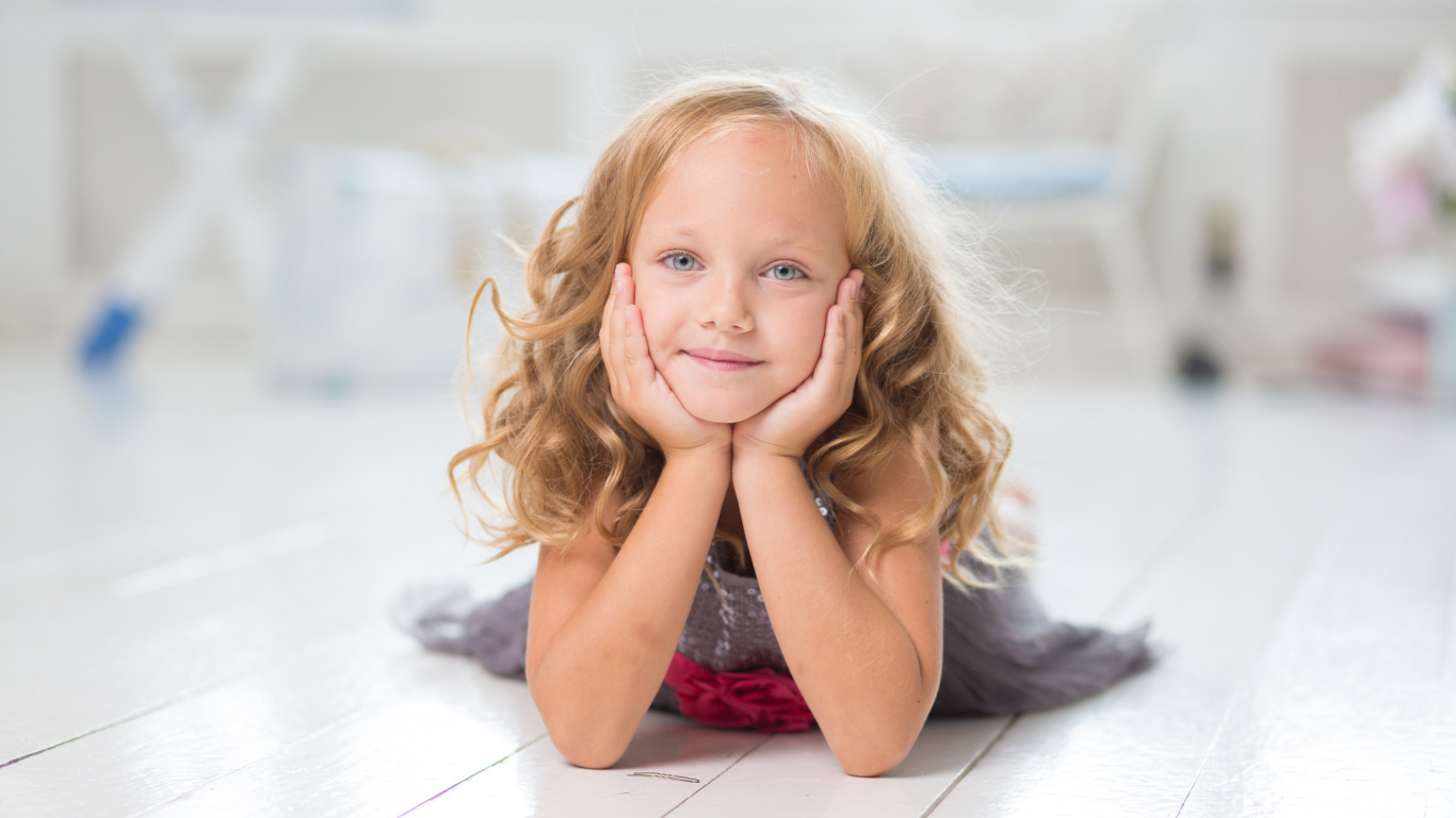 Маленькая длинноволосая голубоглазая девочка лежит на полу