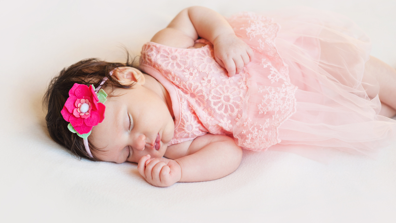Маленькая спящая девочка в розовом платье с цветком в волосах 