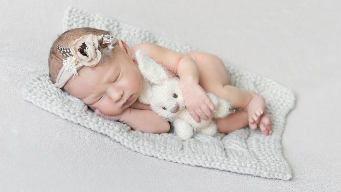 Спящий младенец с игрушкой на сером фоне 