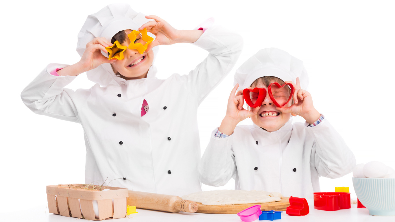 Два маленьких ребенка в костюмах повара готовят на кухне печенье