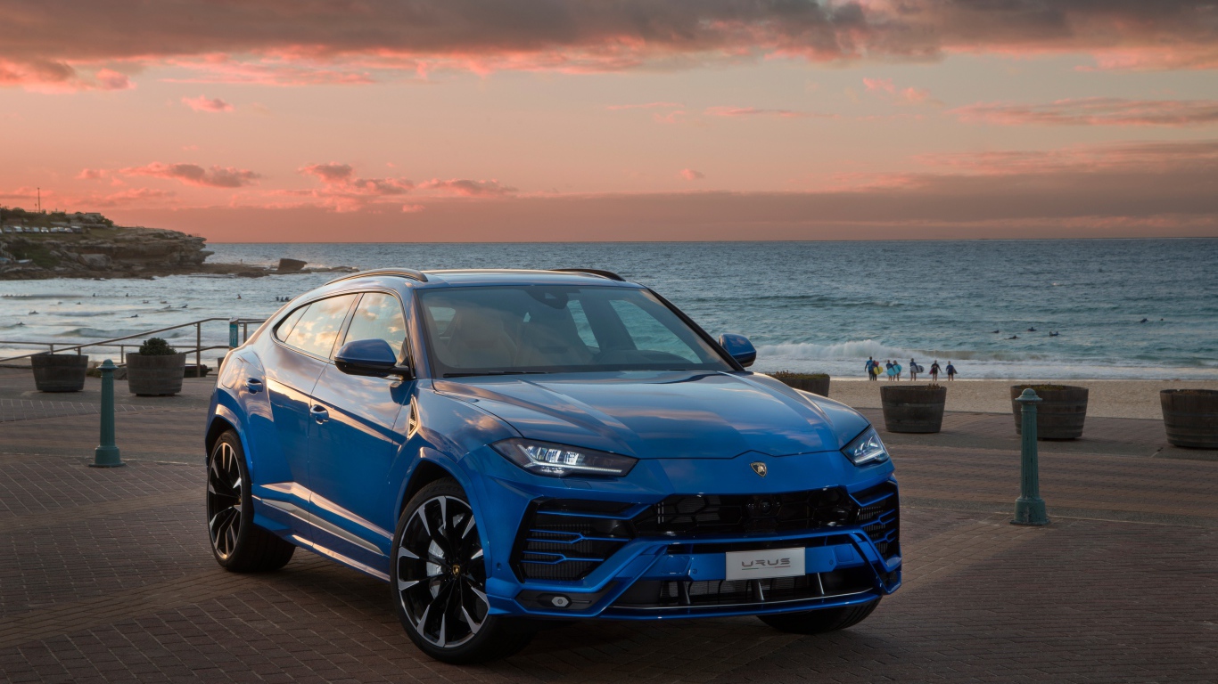 Синий автомобиль Lamborghini Urus под пасмурным небом на берегу  океана