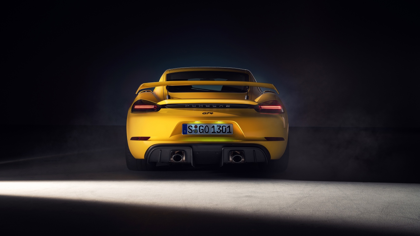 Желтый автомобиль Porsche 718 Cayman GT4, 2019 года вид сзади на сером фоне