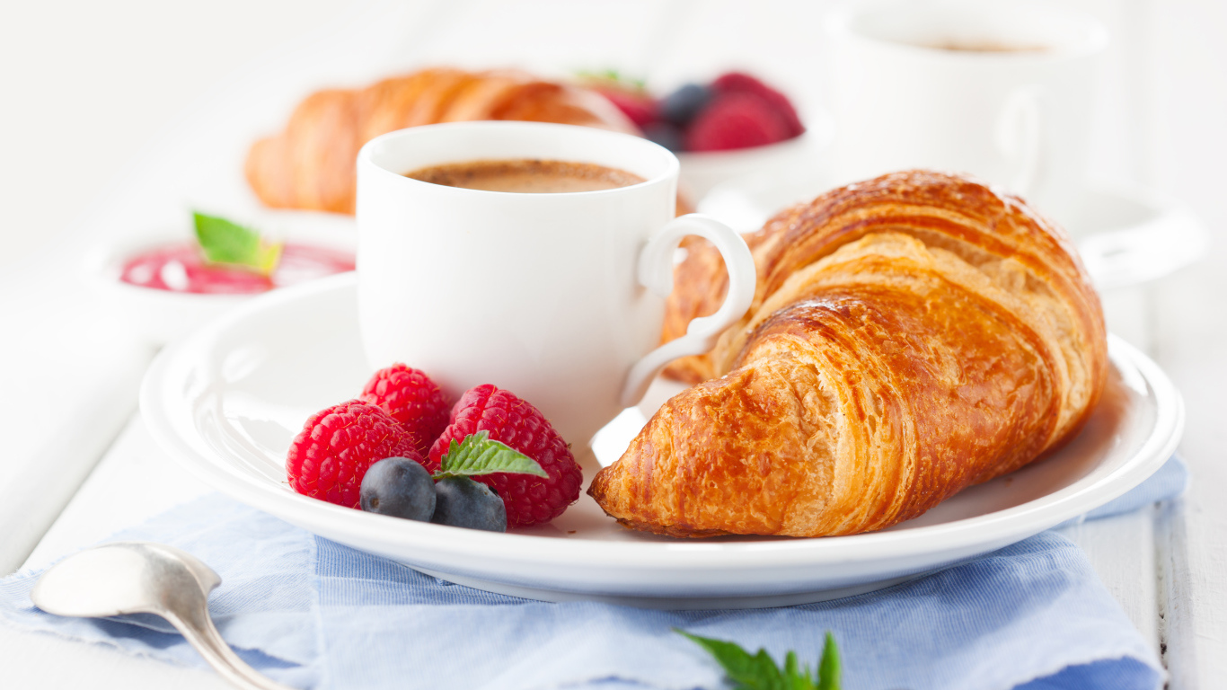 Чашка кофе на тарелке с круассаном и ягодами
