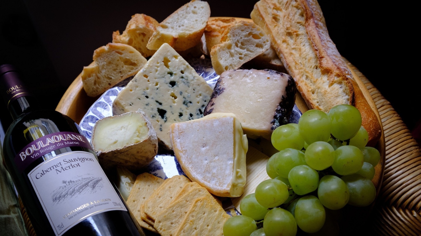 Разные виды твердого сыра на тарелке с белыми виноградом и вином