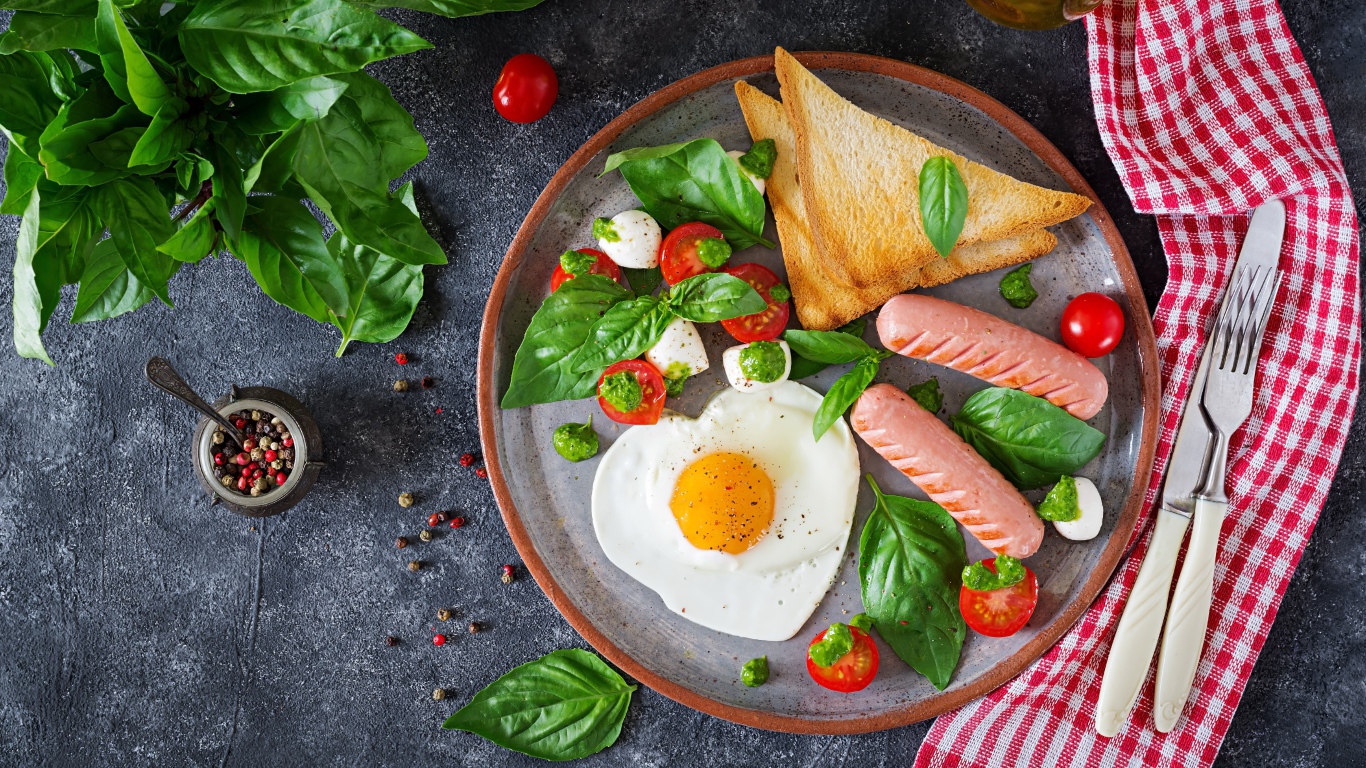 Яичница на тарелке с помидорами, гренками, сыром, сосисками и зеленью базилика