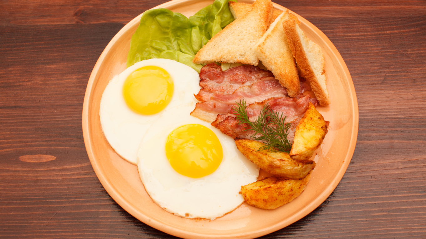 Яичница с беконом, картофелем фри и гренками на столе 