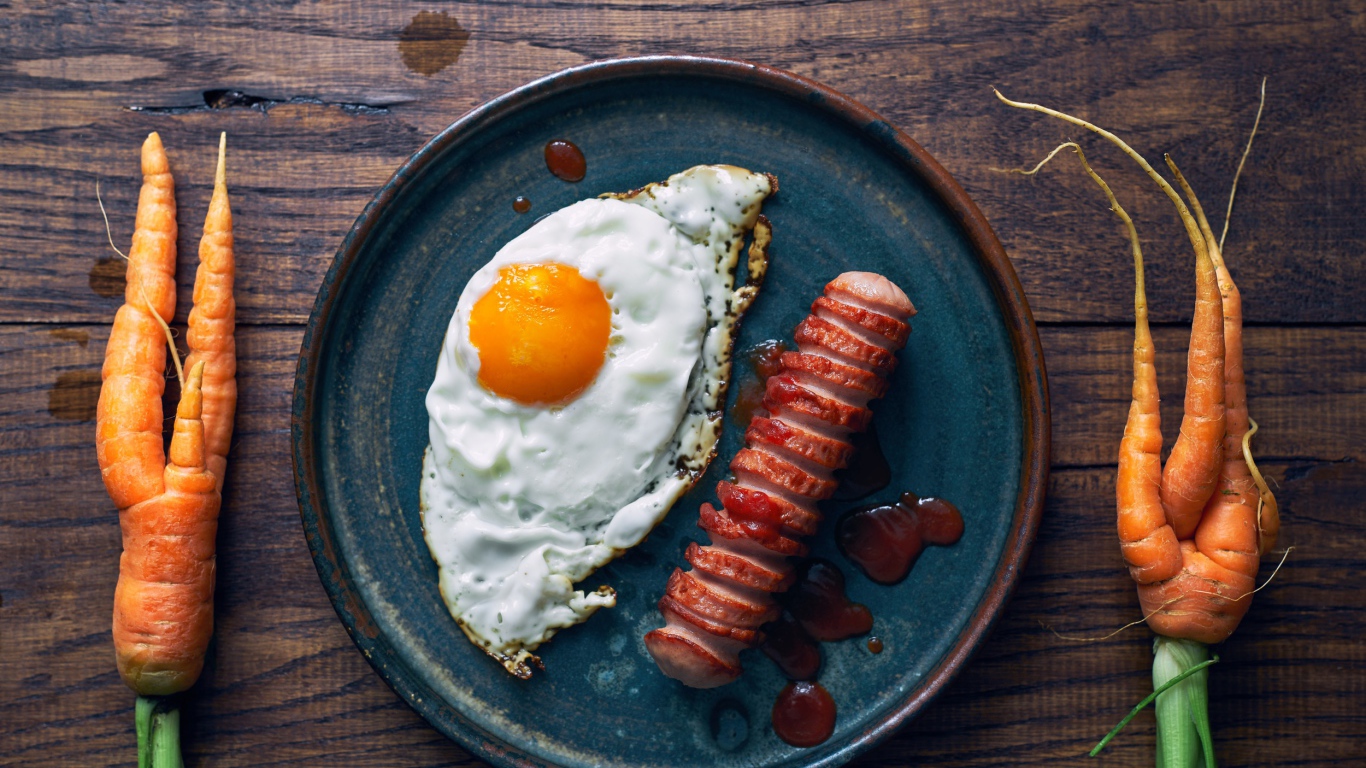 Яичница с сосиской на столе с морковью 