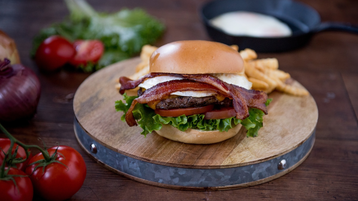 Гамбургер с беконом на столе с овощами