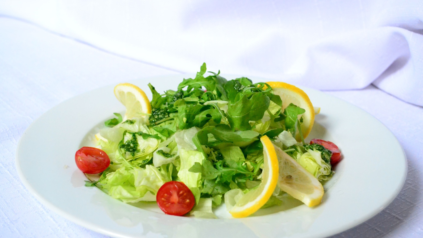 Салат с рукколой, лимоном и помидорами на белой тарелке