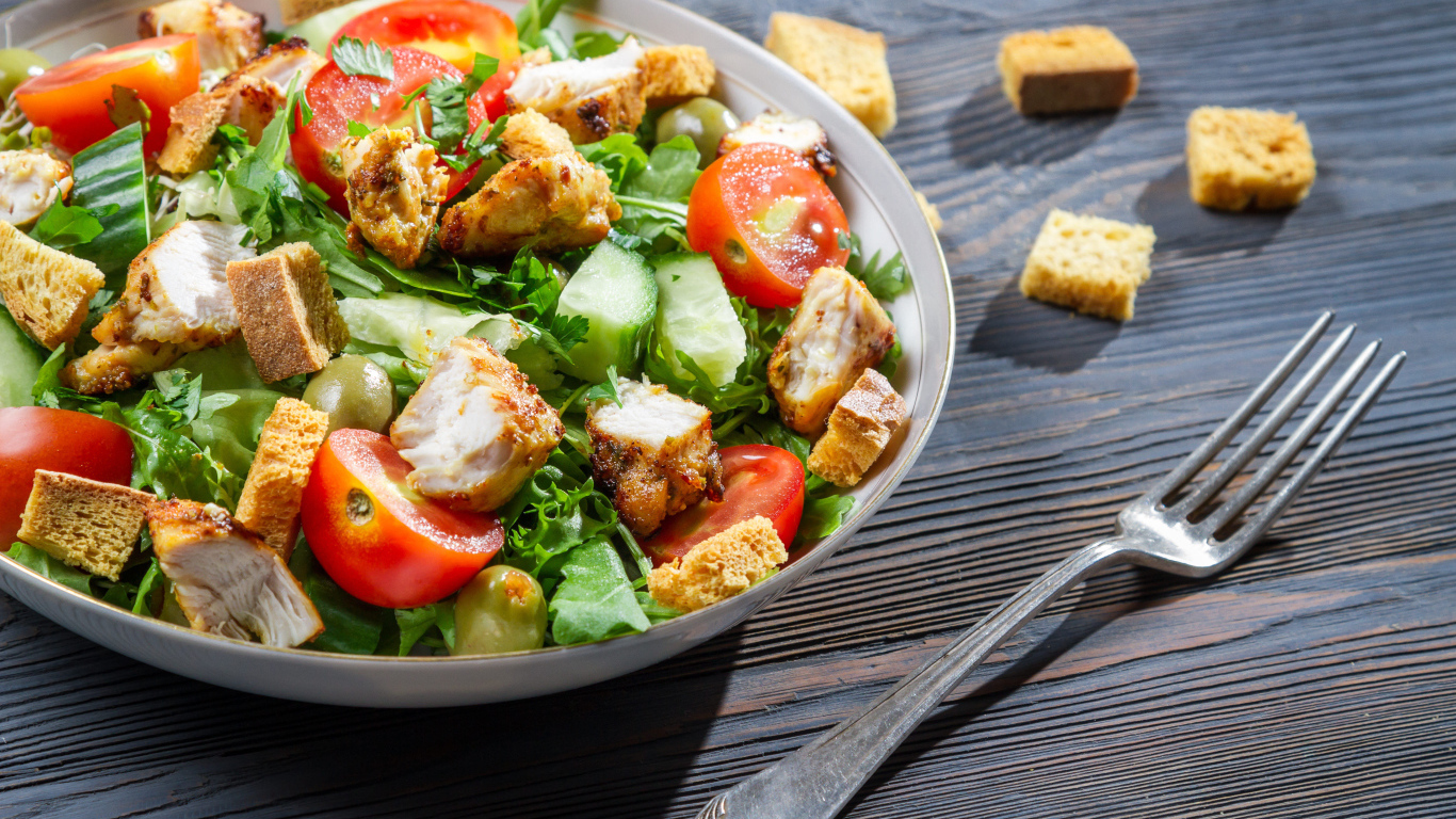 Салат с овощами, сухариками и курицей и на столе с вилкой