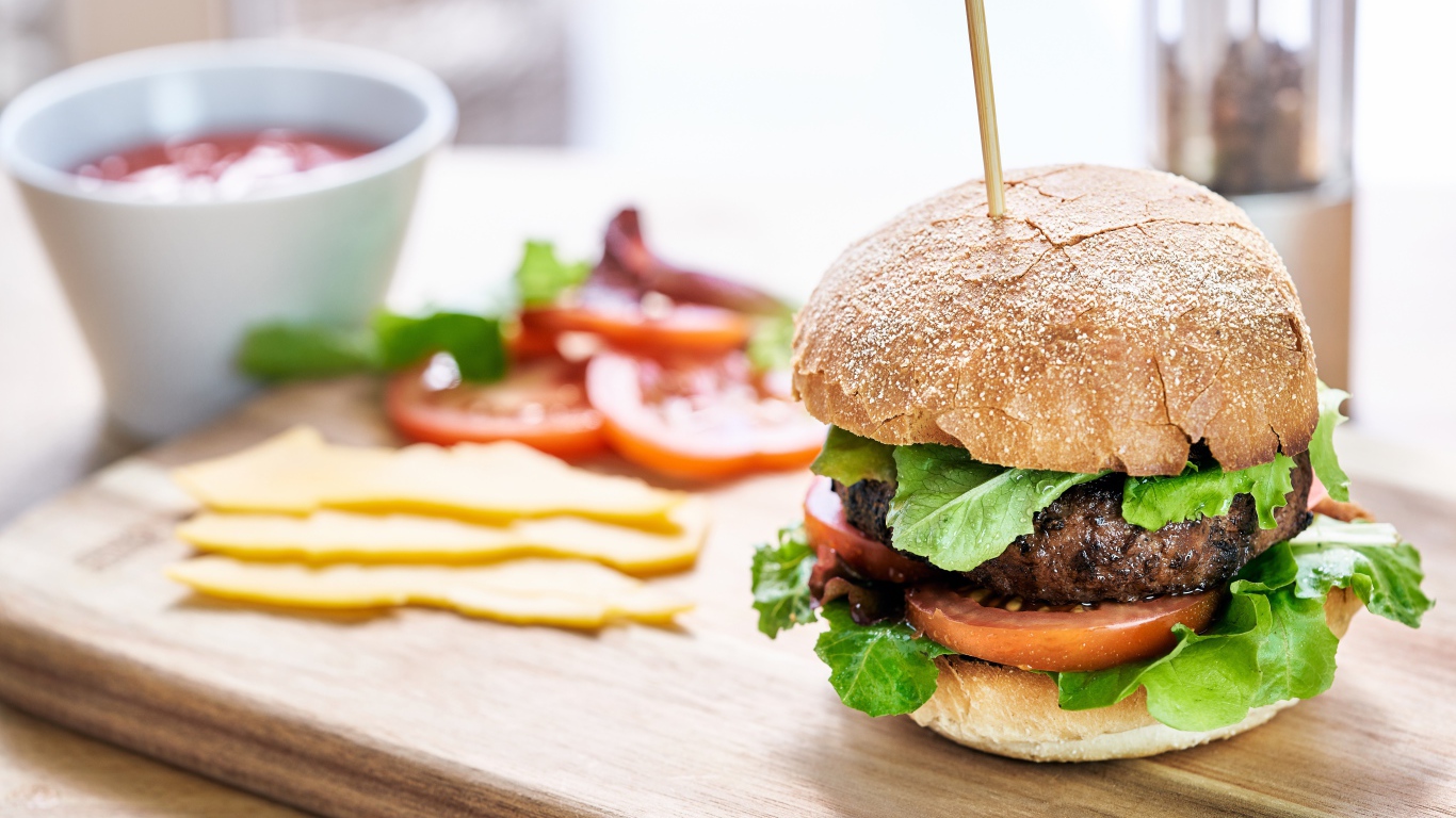 Аппетитный гамбургер на доске с сыром и помидорами