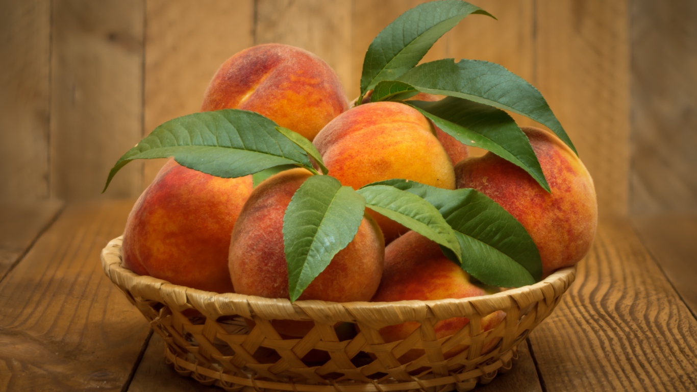 Корзинка персиков с зелеными листьями на столе