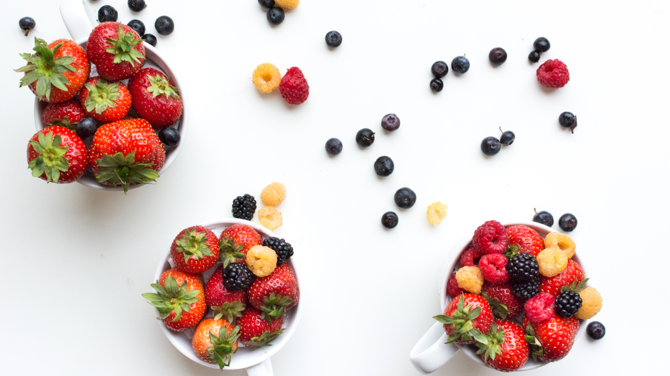 Чашки на столе с ягодами клубники, малины и ежевики 