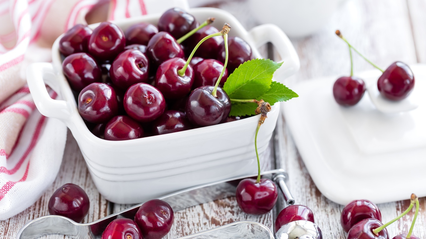 Красные спелые вишни в белой тарелке на столе