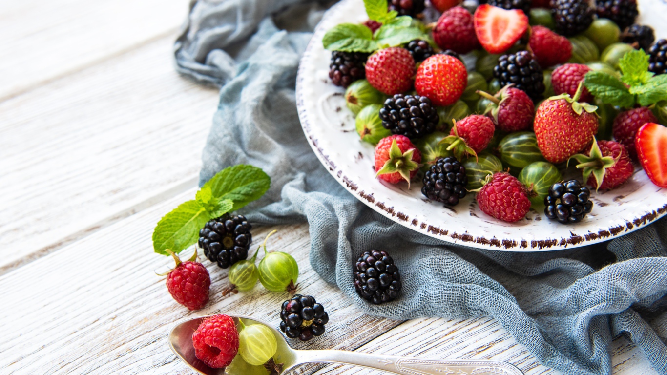 Спелые ягоды крыжовника, ежевики, малины и клубники на тарелке