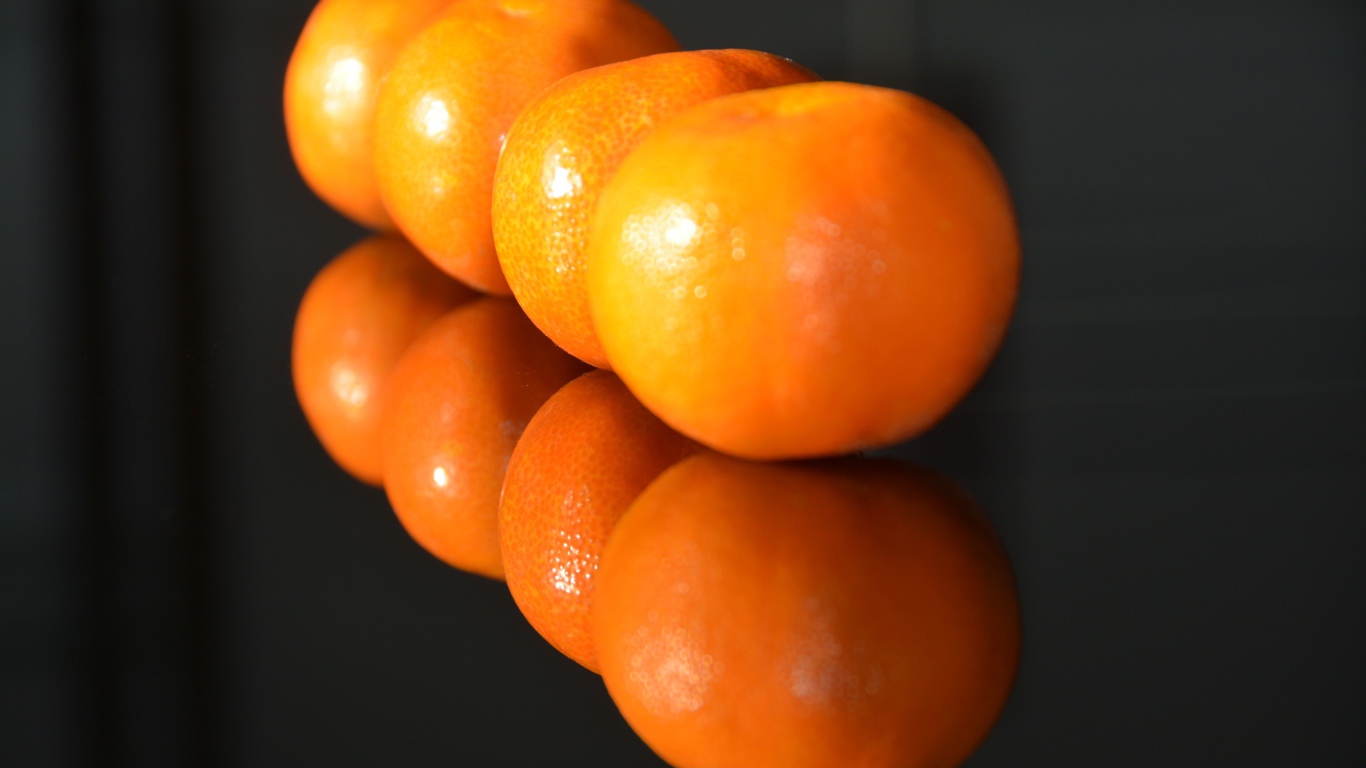 Желтые мандарины отражаются в поверхности стола 