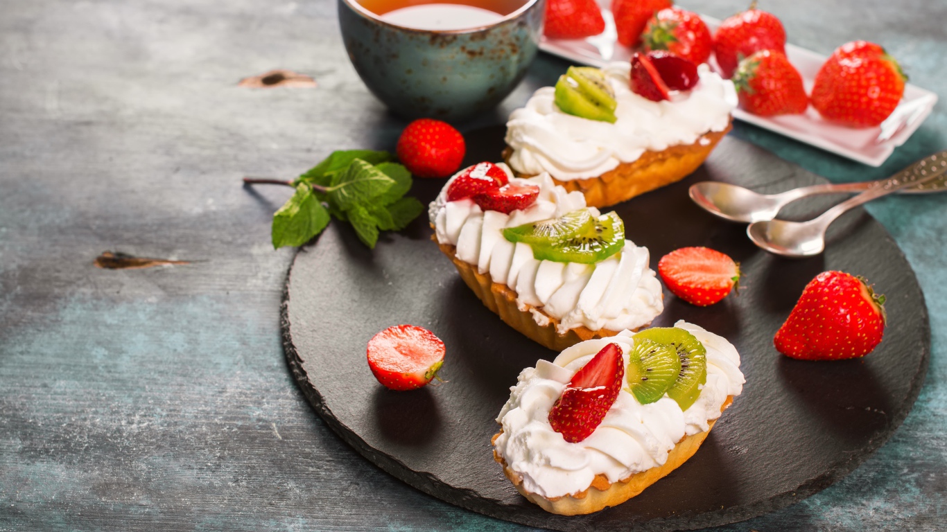 Пирожные с киви и клубникой на столе с чаем