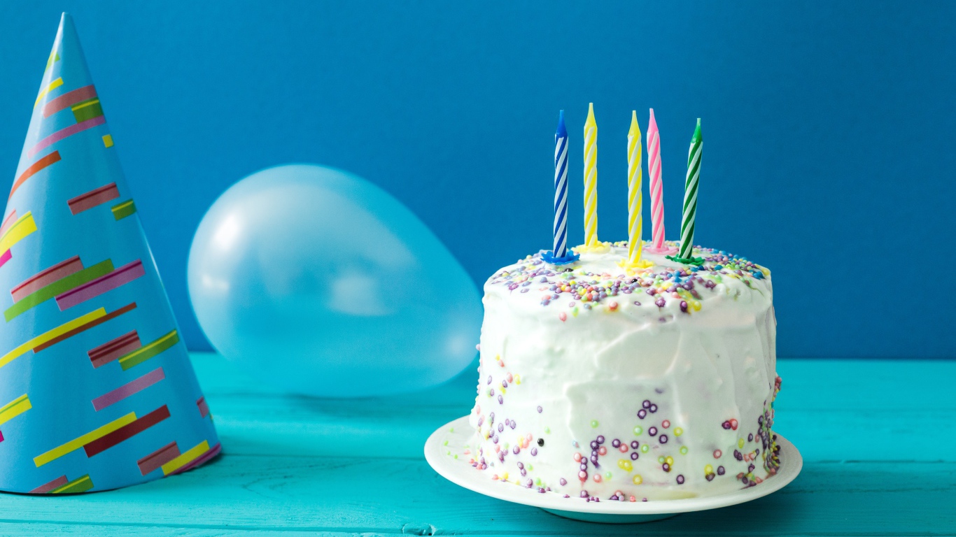 Праздничный торт со свечами, шариком и колпаком на голубом фоне