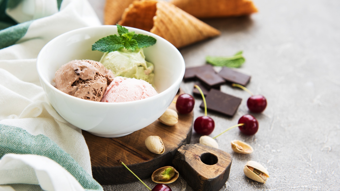 Шарики мороженого на столе вафельными рожками, черешней и фисташками