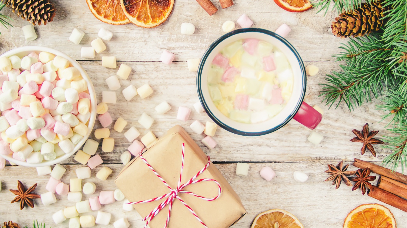 Кружка горячего напитка на столе с маршмеллоу, пряностями и подарком