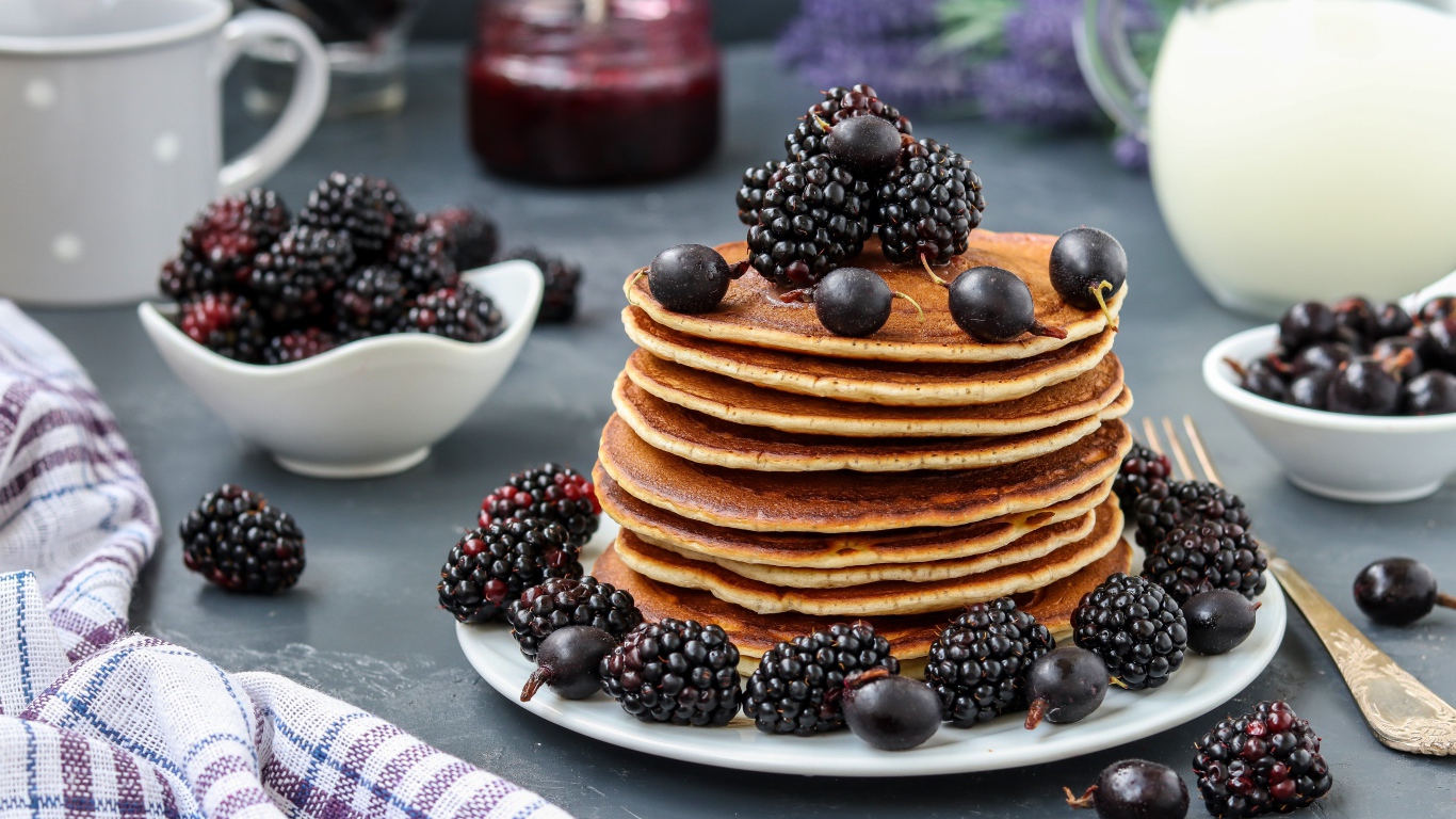 Румяные оладьи на тарелке с ягодами черники и смородины