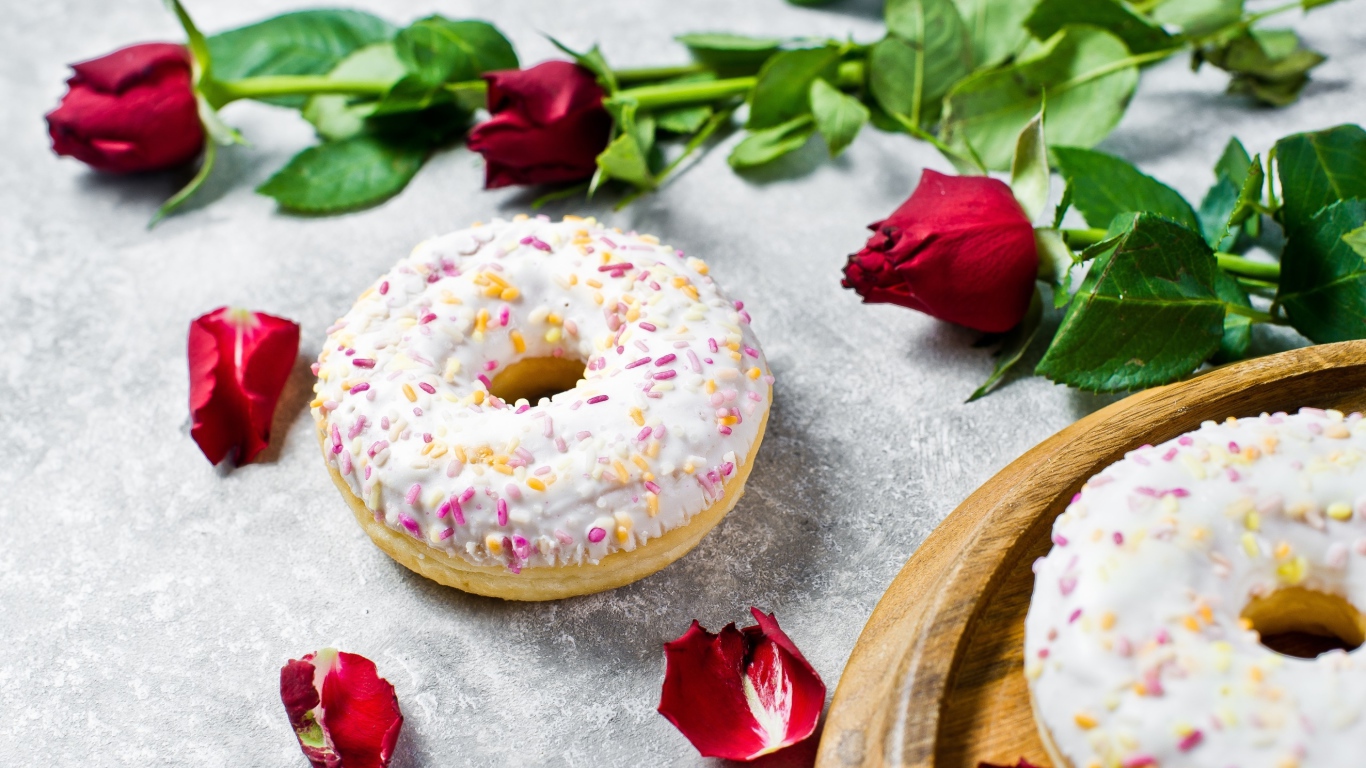 Сладкий пончик с глазурью на столе с красными розами
