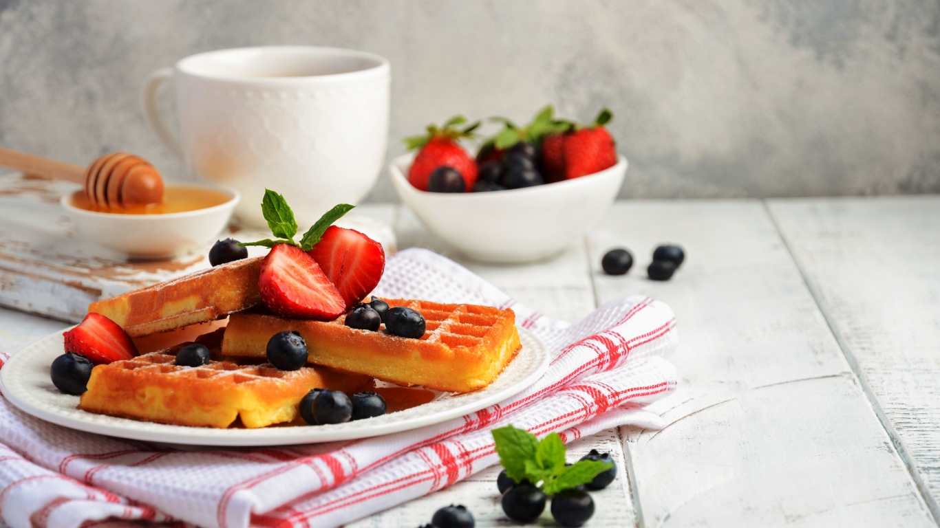 Сладкие вафли с ягодами черники и клубники на столе с медом и чаем