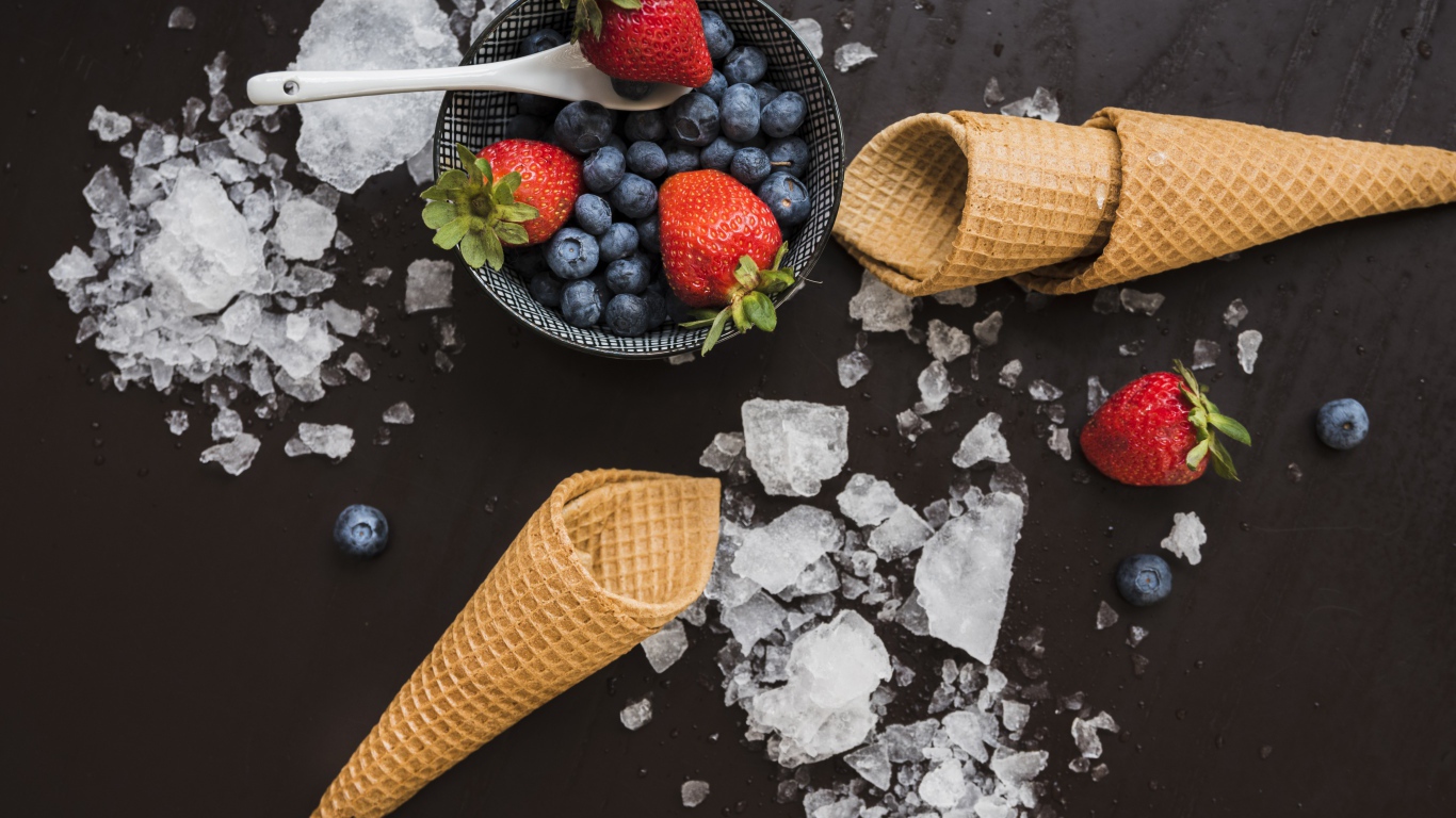 Вафельные рожки на столе со льдом и ягодами черники и клубники