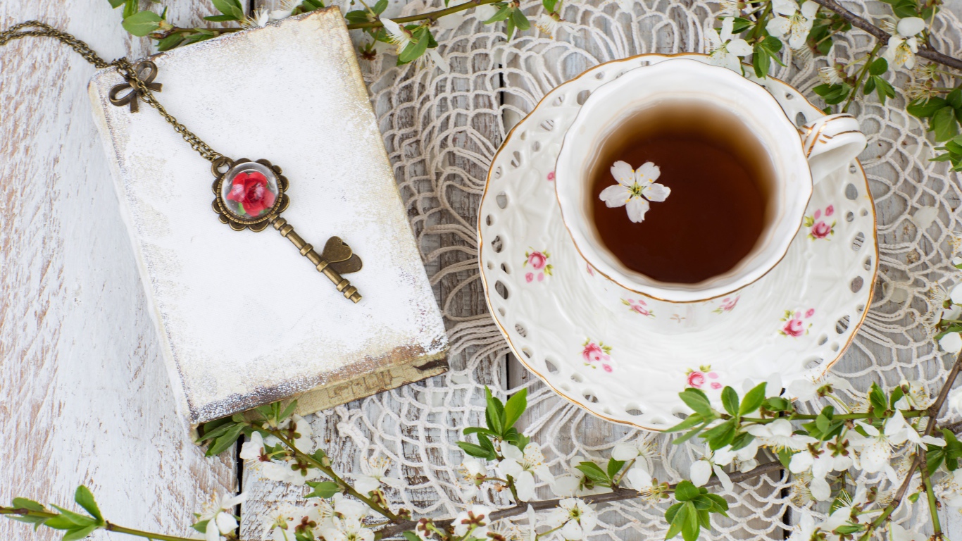Чашка чая на столе с книгой и белыми цветами вишни 