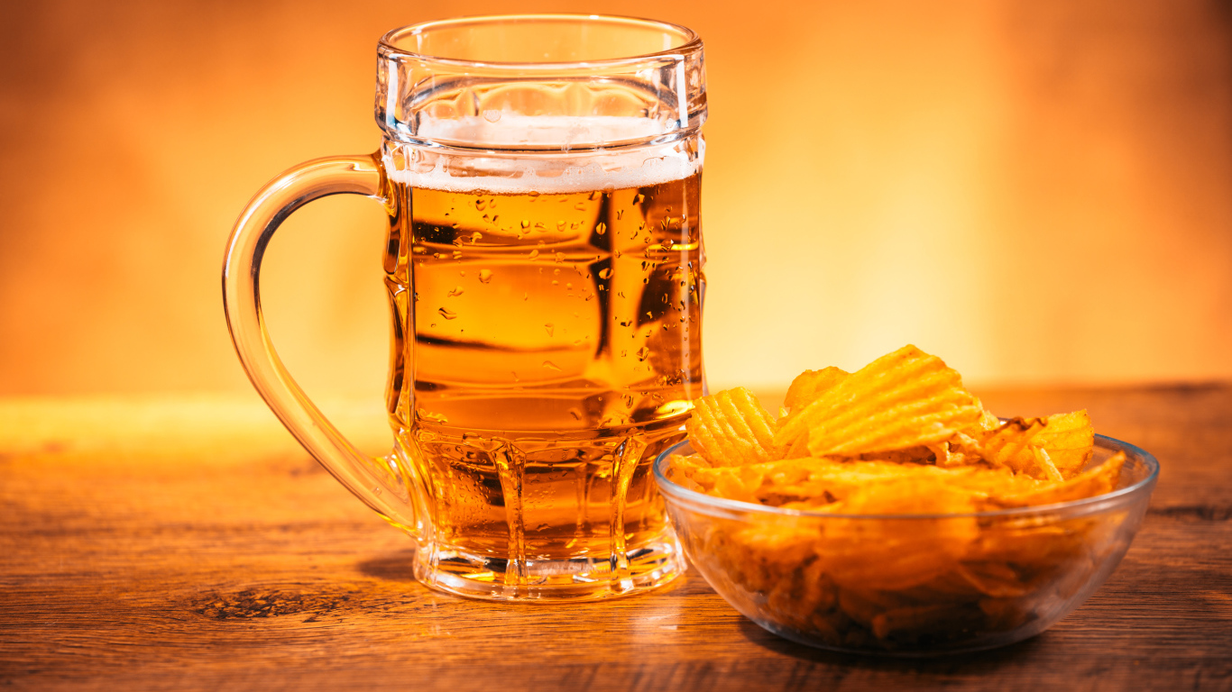 Бокал пива с тарелкой чипсов на столе 