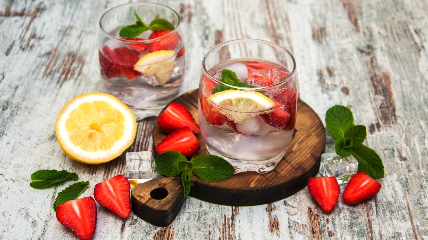 Холодный мохито на столе с ягодами клубники, лимоном и мятой