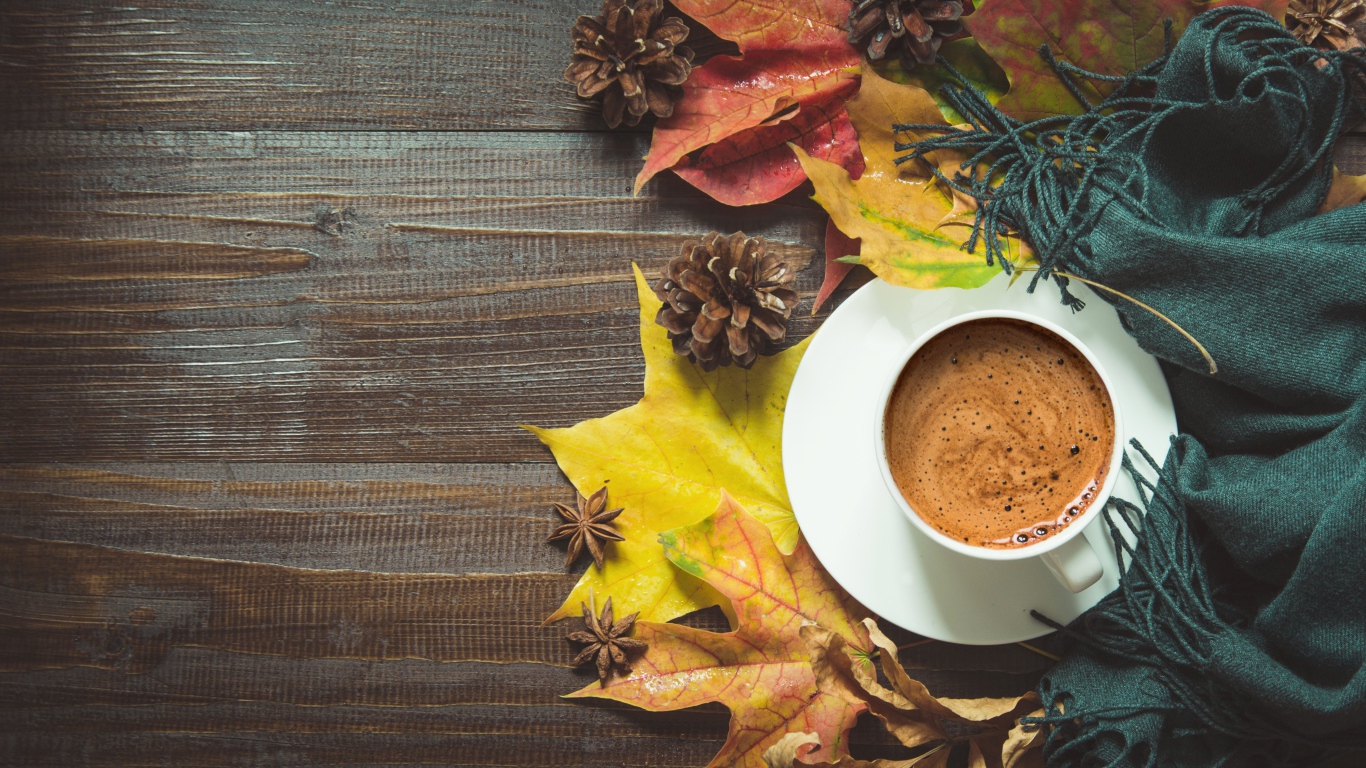 Чашка кофе на столе с шарфом, желтыми листьями и шишками