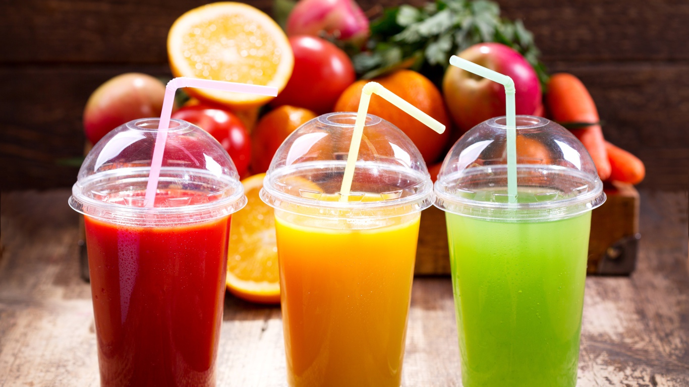 Свежие соки в стаканах с трубочками на столе