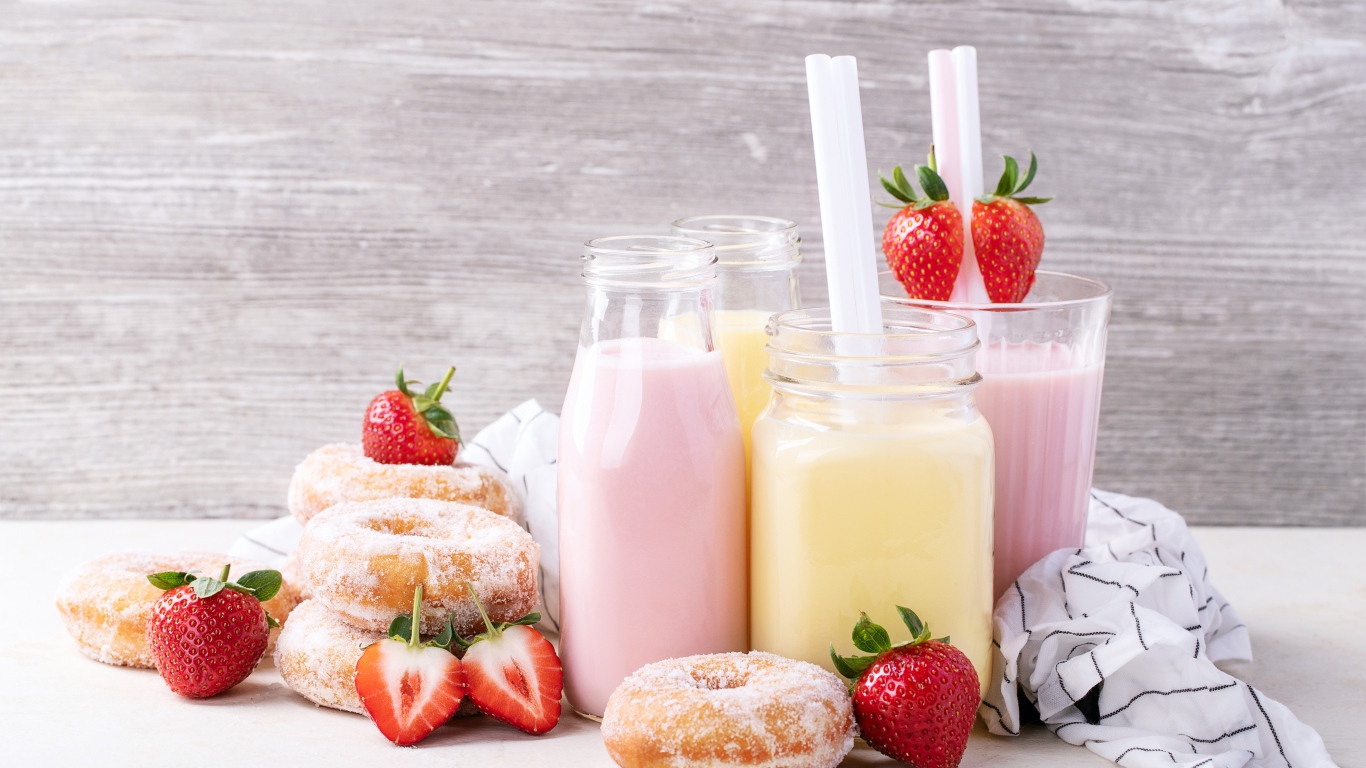 Молочные коктейли на столе с пончиками и ягодами клубники 