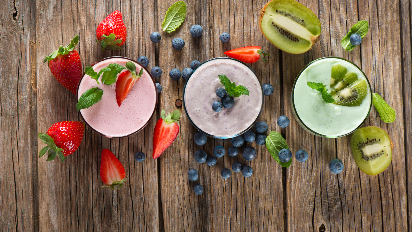Стаканы со смузи на столе с киви, ягодами клубники и черники