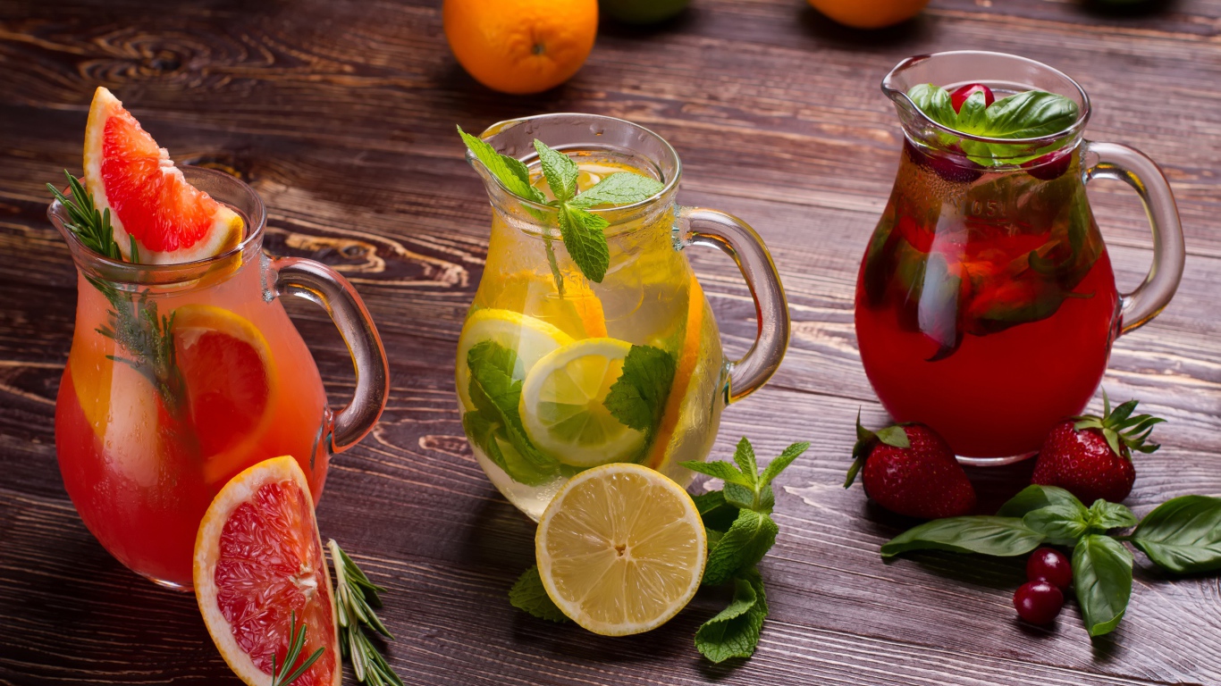 Три стеклянных графина с напитком на деревянном столе с фруктами