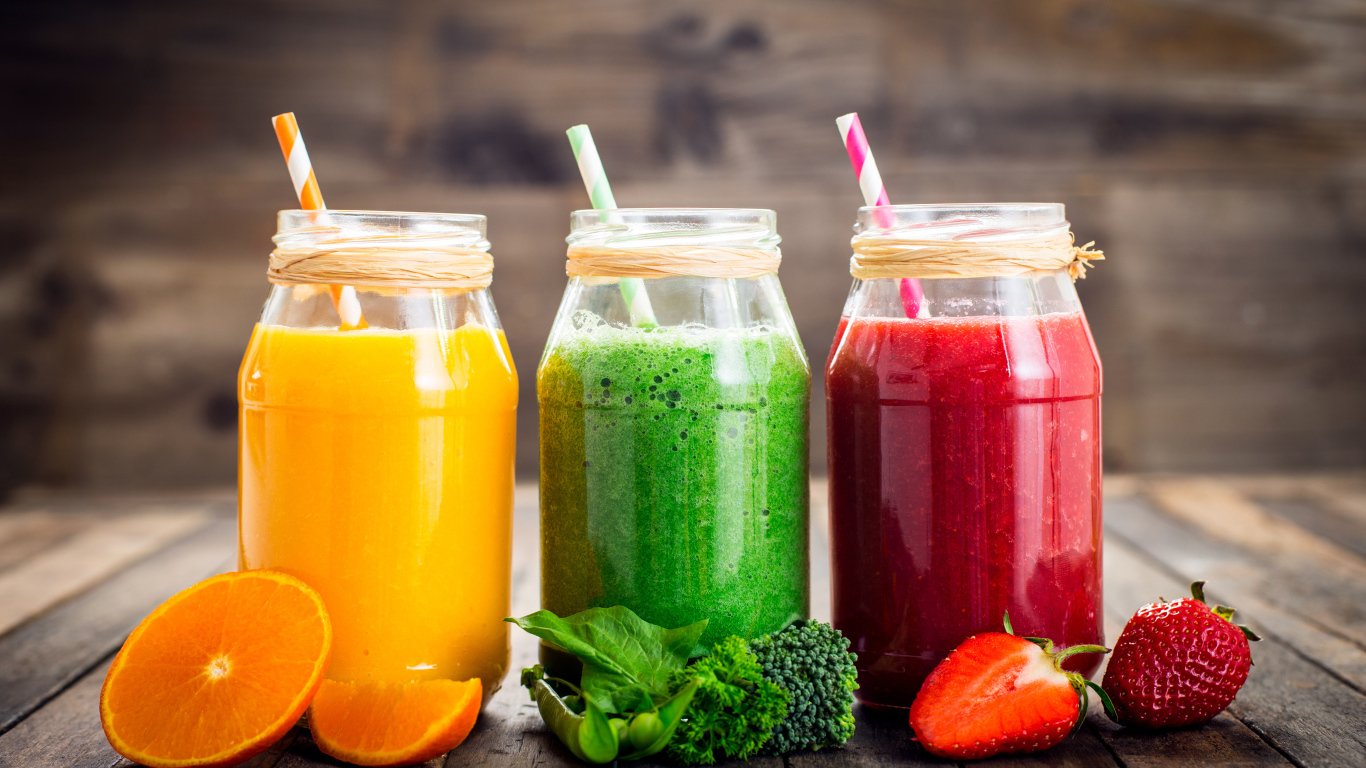 Три банки смузи с трубочкой на столе с апельсином, брокколи и клубникой