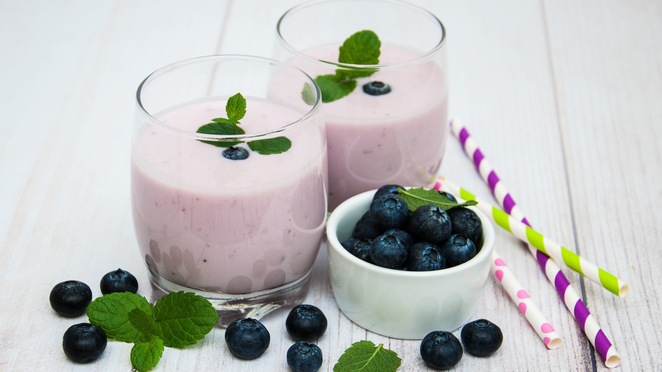 Два стакана коктейля в стаканах на столе с ягодами черники и трубочками