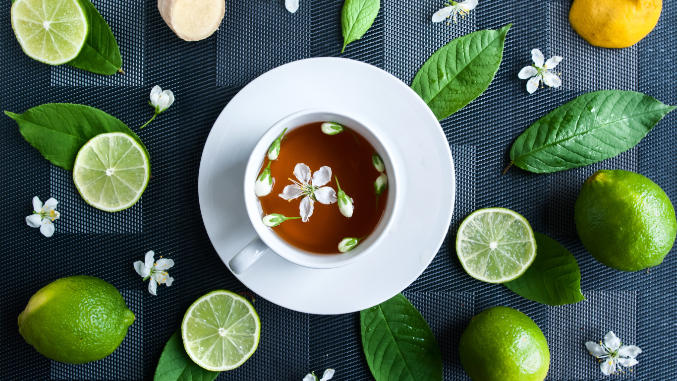 Белая чашка с чаем на столе с лаймом и зелеными листьями 