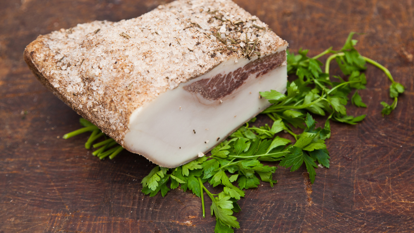 Кусок сала со специями на столе с зеленью петрушки