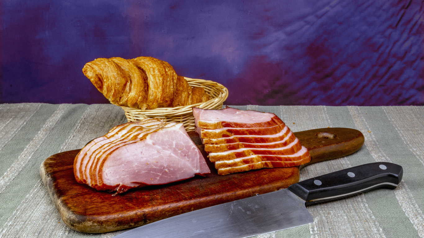Кусок нарезанной ветчины на доске с круассаном