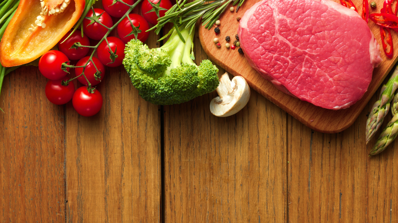 Кусок свежего мяса на столе с овощами и зеленью 